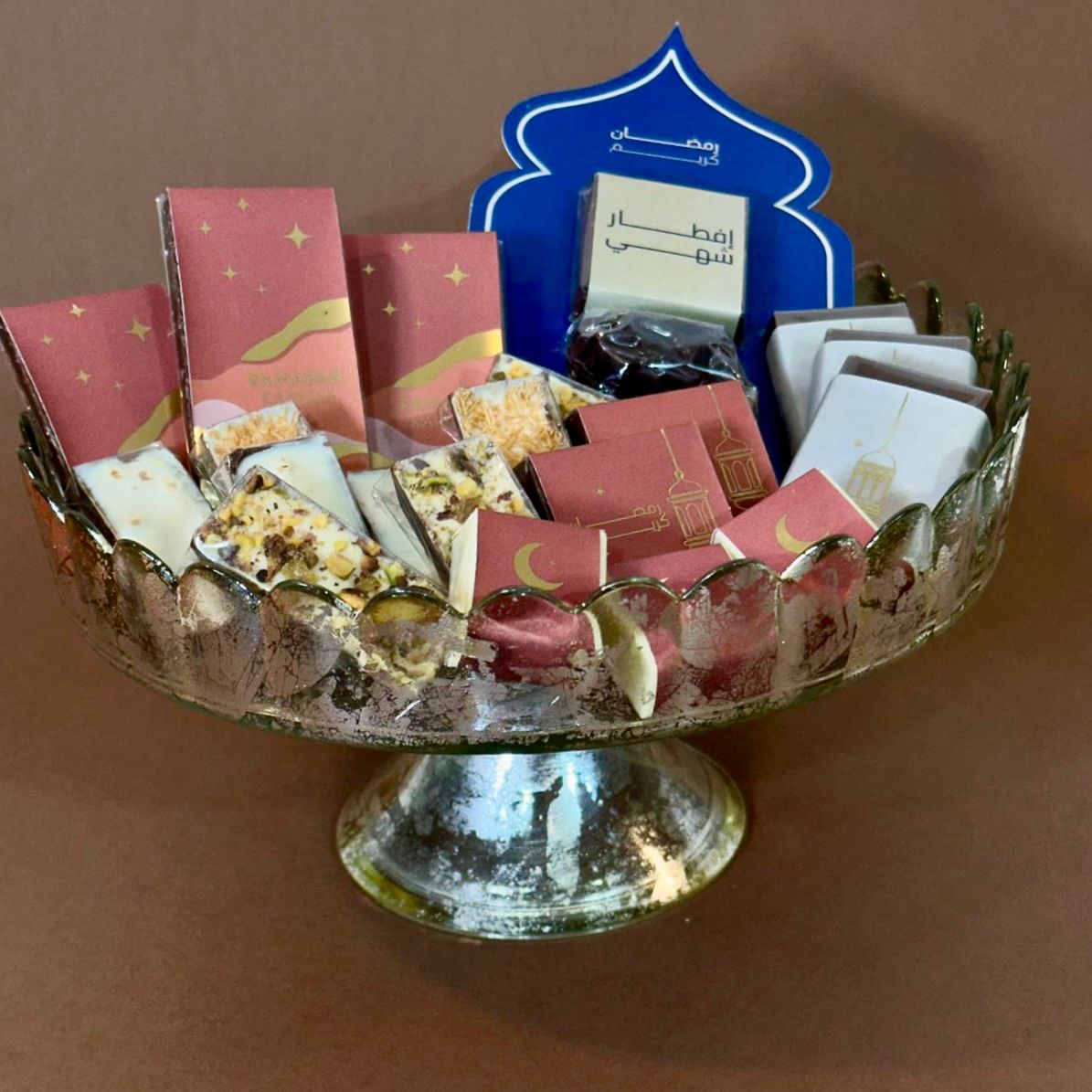 Decorative bowl with chocolate pieces and a blue Ramadan motif item on a brown background