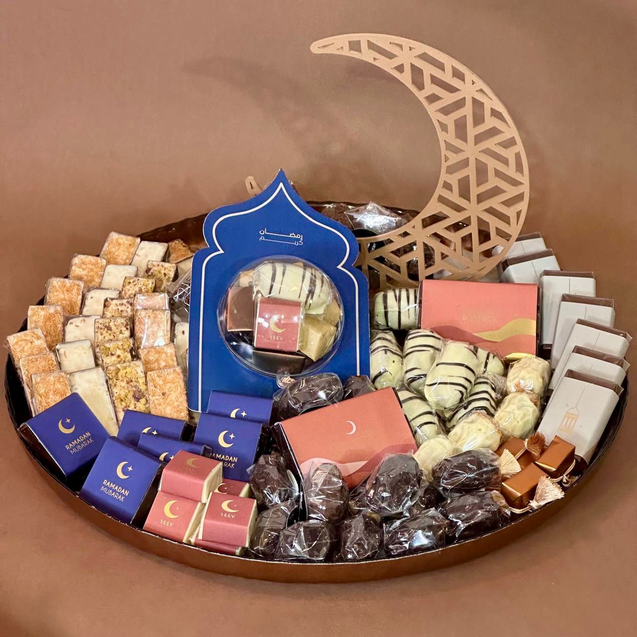 Assorted Ramadan sweets and pastries on a tray with a decorative moon symbol on a brown background