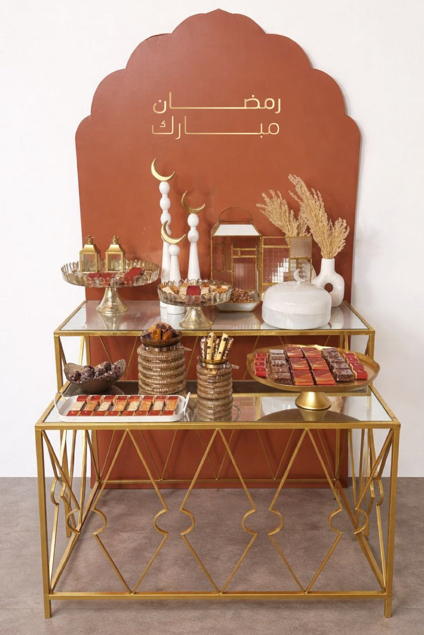 Decorative table with gold frame and glass top against a white wall with ramadan chocolate display Arabic text.
